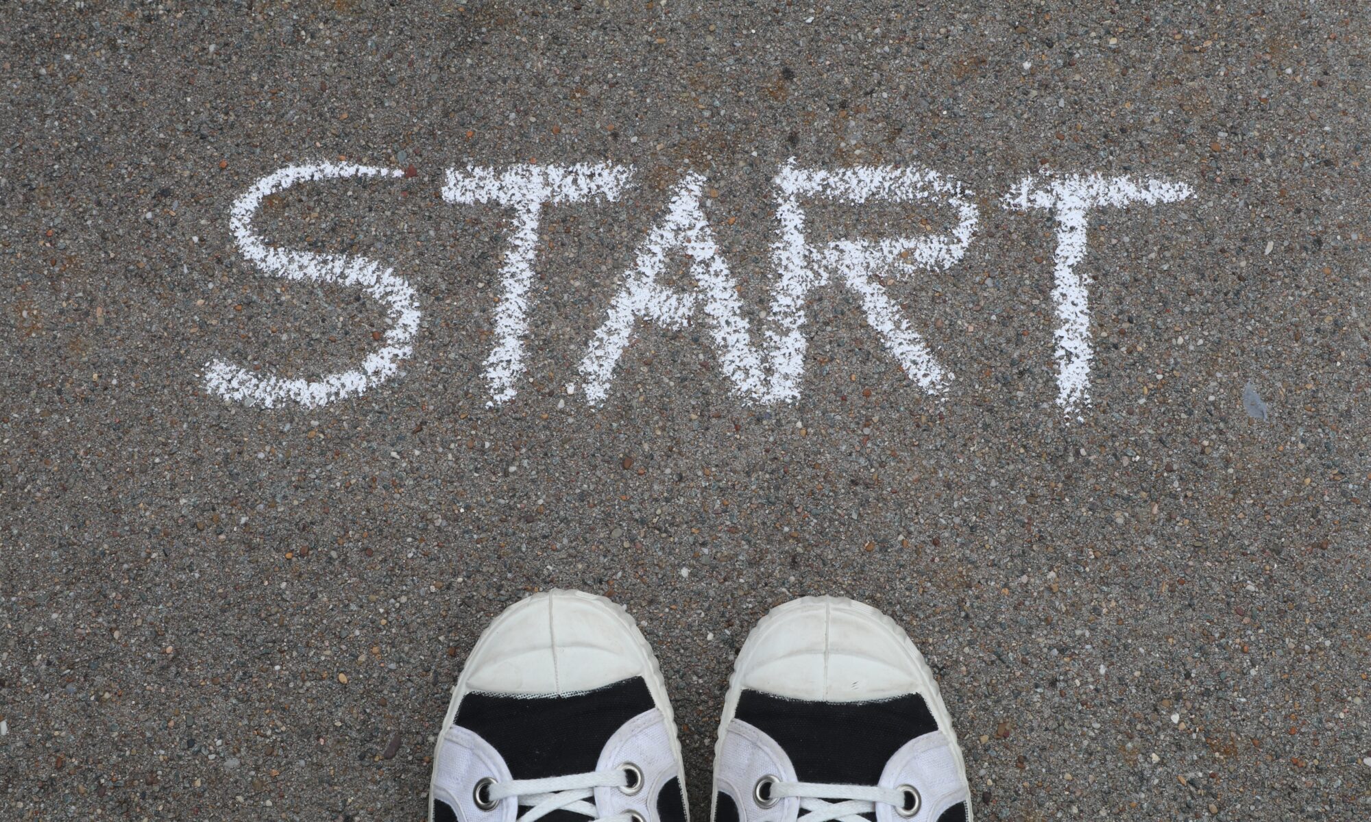 Looking down at "START" written in chalk on sidewalk, with shoes of photographer under it.